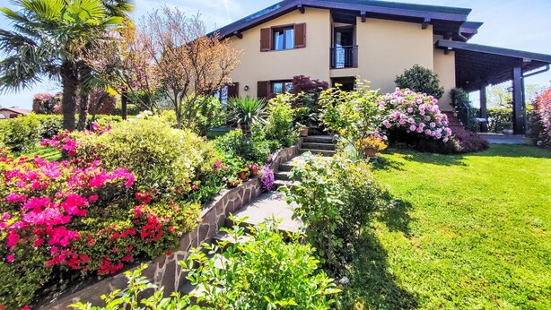 Una casa de dos pisos con un porche cubierto, rodeada de un jardín cuidado con diversas plantas y flores.