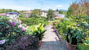 Un sendero en un jardín que conduce a una casa con paneles solares en el techo, rodeada de exuberante vegetación y plantas en flor.