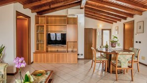 Un salón amplio con techo de madera, un televisor sobre un mueble de madera, una mesa de comedor con sillas y una orquídea en maceta.