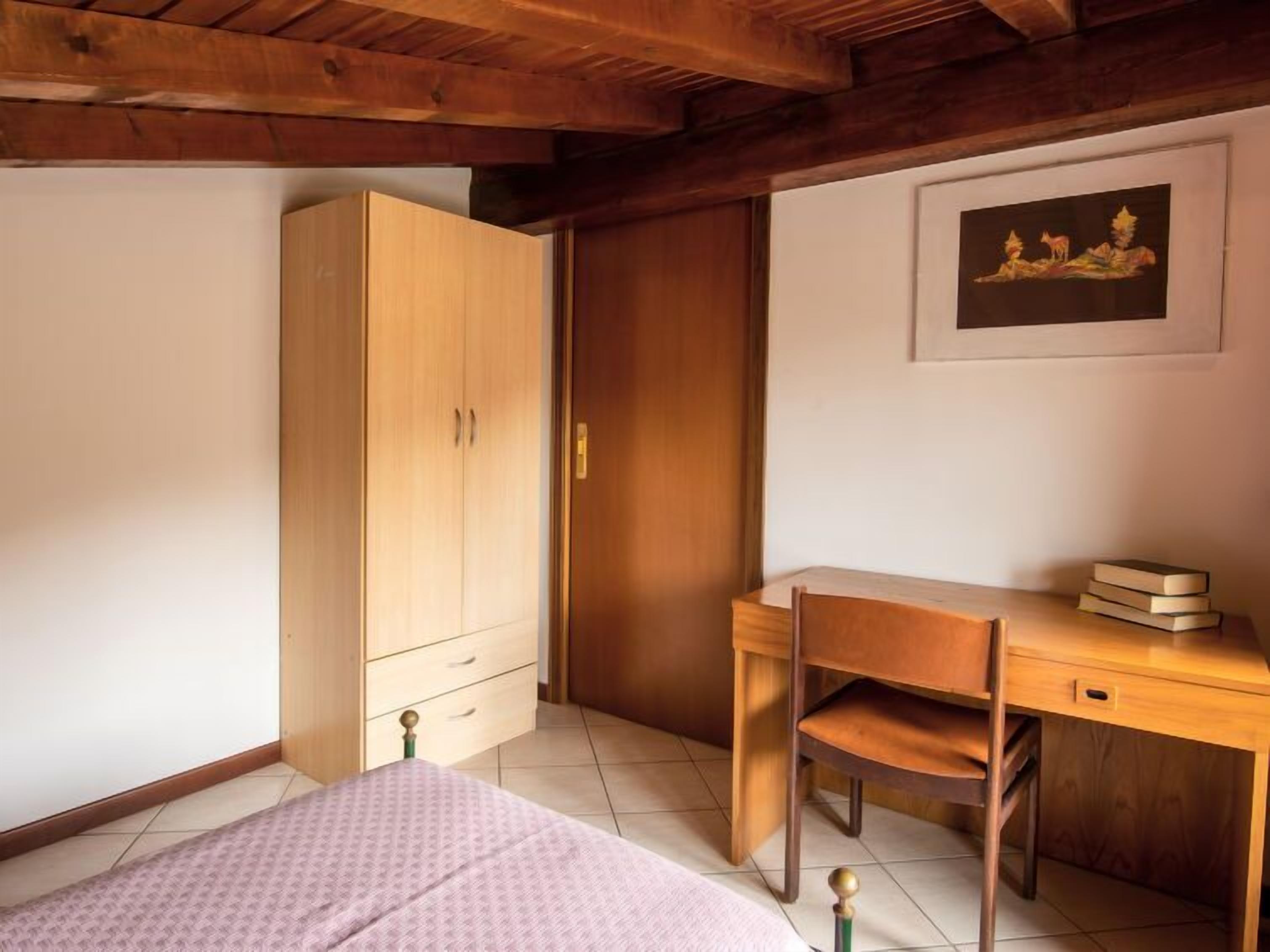 Um quarto com uma cama, uma escrivaninha de madeira, um guarda-roupa e um quadro na parede.