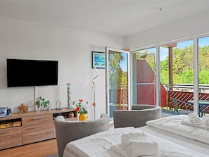 A hotel room with a bed, a desk, a TV, a window with a view of trees, and a balcony. - Düneneck App.17 by Interhome (Zempin)