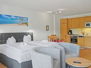 A hotel room with a bed, two armchairs, a small round table, a kitchenette, and a painting of a beach scene. - Düneneck App.17 by Interhome (Zempin)
