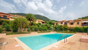 Une piscine entourée d’une terrasse carrelée, avec une chaîne de montagnes en arrière-plan et des immeubles résidentiels.