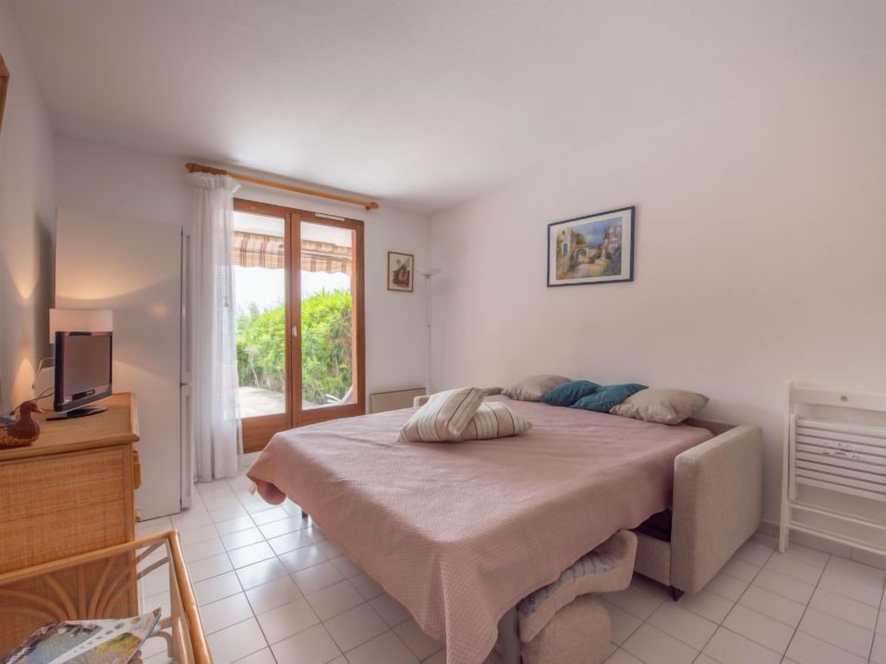 A bedroom with a bed, a desk with a computer, a chair, and a window with curtains.
