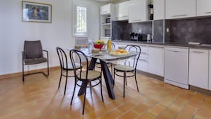 Una cocina moderna con armarios blancos, una mesa de comedor con sillas y una ventana con persianas.