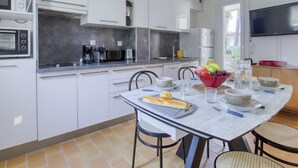 Una cocina moderna con armarios blancos, una mesa de comedor con sillas y un televisor montado en la pared.