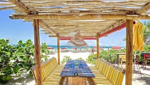 A beachside outdoor seating area with a wooden pergola, a table with chairs, and a view of the beach and ocean. - Hello Summer! beachfront studio in the heart of Orient Bay, pool direct access (Orient Bay)