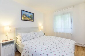 A bedroom with a bed, two bedside tables, a nightstand, a painting on the wall, and a window with curtains. - Holiday house DUNJA with private pool (Omišalj)