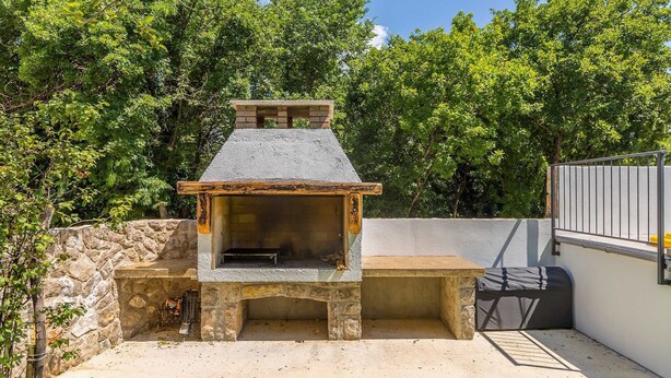 Zona de barbacoa al aire libre de piedra con chimenea, rodeada por un muro de piedra y un césped.
