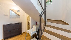 Una escalera con escalones de madera y barandillas de metal, un aparador de madera oscura, una silla blanca y una pequeña mesa con una cesta.