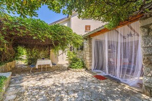 A stone courtyard with a table and chairs, a covered seating area, and a building with a stone facade. - Holiday house DUNJA with private pool (Omišalj)
