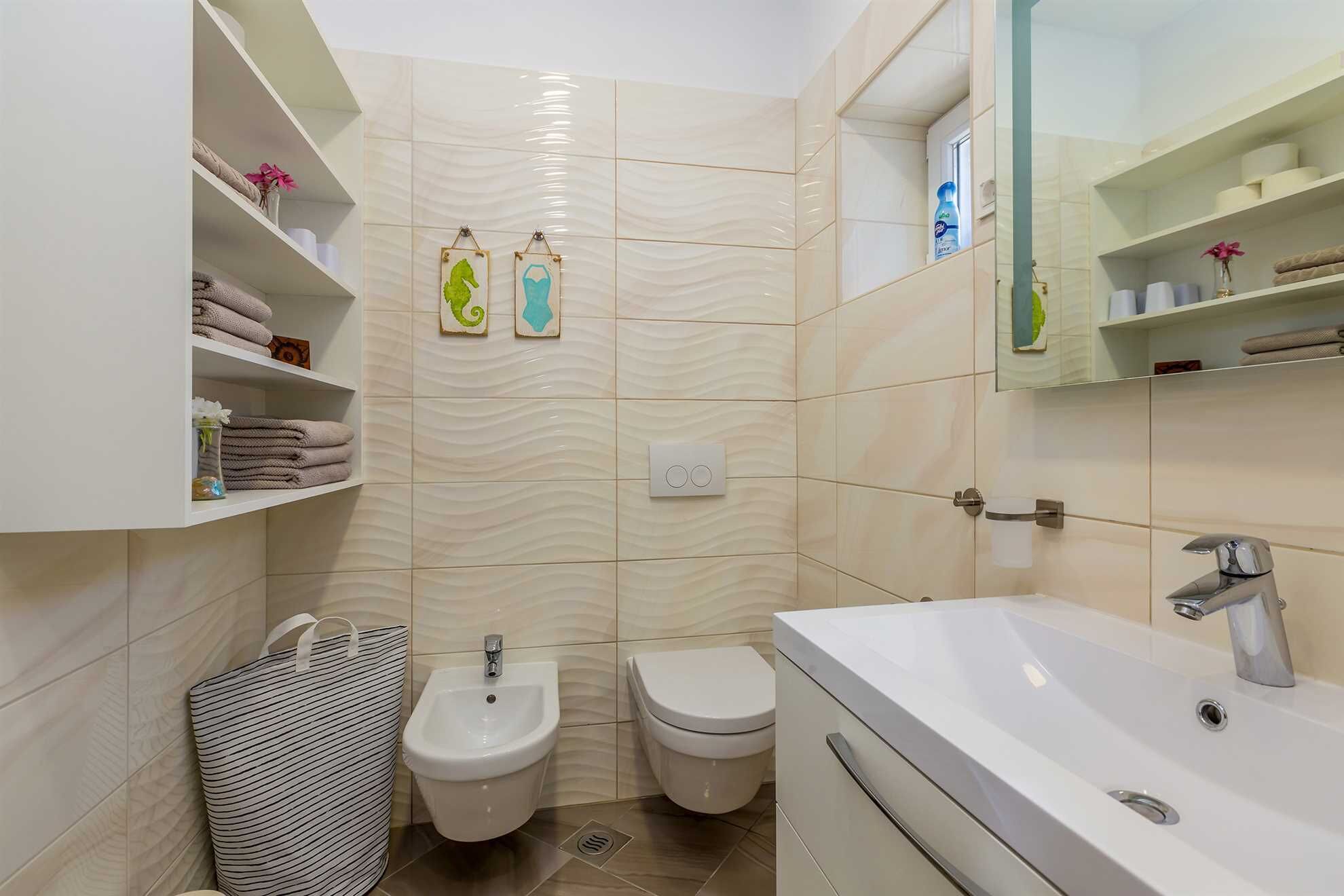 Ein modernes Badezimmer mit integriertem Bidet, Toilette und Waschbecken. Handtücher und Pflegeprodukte stehen auf Regalen bereit.