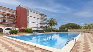 Una piscina con borde de baldosas, rodeada por un edificio de varios pisos con balcones.