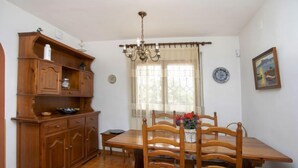 A dining area with a wooden table and chairs, a chandelier, and a window with curtains. - Vacation home Marie by Interhome (L'Escala)