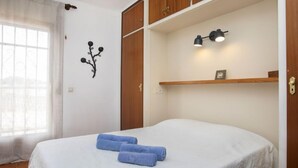 A bedroom with a bed, a window with curtains, a wall-mounted lamp, and a shelf with a picture. - Vacation home Marie by Interhome (L'Escala)