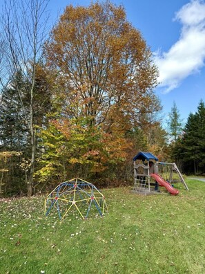 A playground with a slide and climbing structures, surrounded by trees with autumn foliage. - Dome #2 – Located in the Heart of Nature (Saint-Gabriel-de-Valcartier)