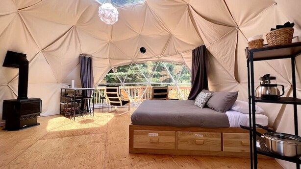 A tented accommodation with a bed, a table, chairs, a stove, and a view of trees. - Dôme #2 Situé en pleine nature (Saint-Gabriel-de-Valcartier)