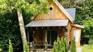Een houten hut met een veranda, omgeven door bomen en een grindpad dat naar de ingang leidt.