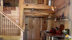 Een houten interieur met een trap, een bank, een eettafel en een keukenhoek.