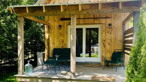 Een houten chalet met een overdekte veranda, twee groene stoelen en een kleine tafel met een fles erop.