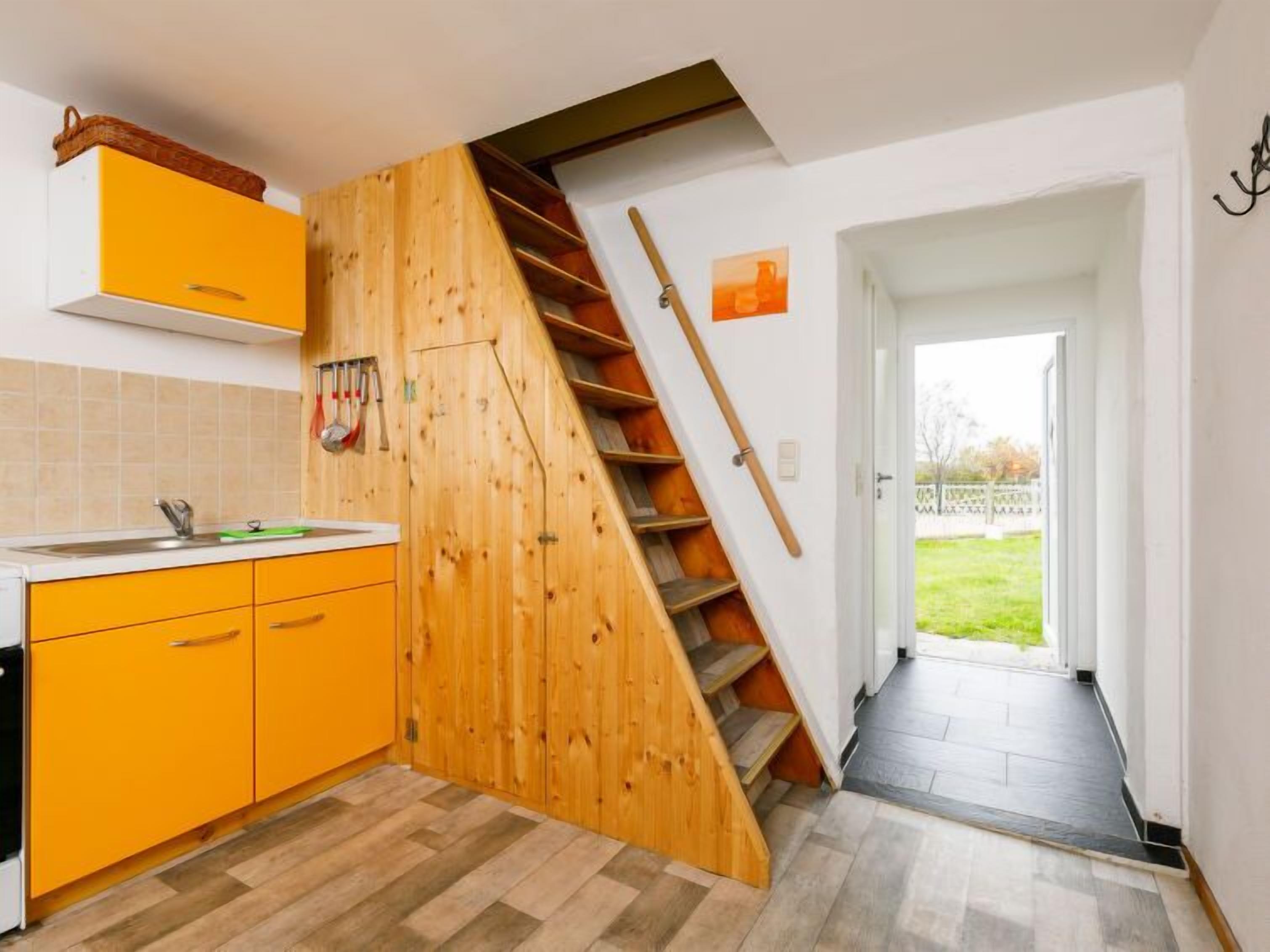 A kitchen with yellow cabinets, a wooden staircase, and a view of a garden through an open door.