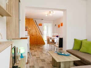 A modern living room with a wooden staircase, a dining area, and a sofa with green cushions.