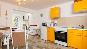 A compact kitchen with yellow cabinets, a white stove, and a dining area with a table and chairs. - Ruprecht by Interhome (Zinnowitz)