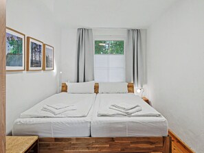 Un lit double avec du linge de lit blanc, une tête de lit en bois et une fenêtre avec des rideaux.
