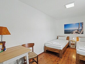 Une pièce avec un plancher en bois, un lit, un bureau, une chaise, une table de chevet, une lampe et un tableau représentant un voilier sur la mer.