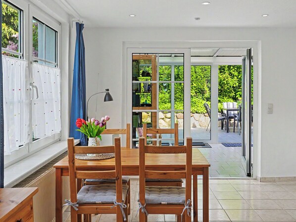 A dining area with a wooden table and chairs, a vase with flowers, and a view of an outdoor patio with a table and chairs. - Usedomer Seekiste by Interhome (Zinnowitz)