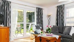 Ein modernes Wohnzimmer mit einer Holzkiste, einem grauen Sofa und einer Glastür, die zu einem Garten führt.