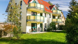 Ein zweistöckiges Haus mit rotem Ziegeldach, grünen Balkonen und einem kleinen Garten mit Außenmöbeln.