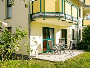 A corner building with a balcony, a small patio with chairs, and a garden area.