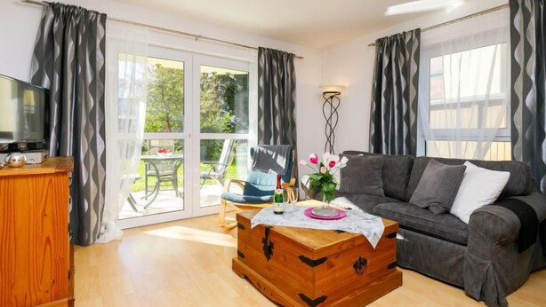 Ein Wohnzimmer mit grauem Sofa, einer Holzkonstruktion, einem Fernseher und einem Essbereich mit Tisch und Stühlen.