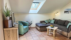 A cozy loft-style living space with a sloped ceiling, a skylight, a green armchair, a sofa, a small wooden table, and a potted plant. - Zaunkönig by Interhome (Zinnowitz)