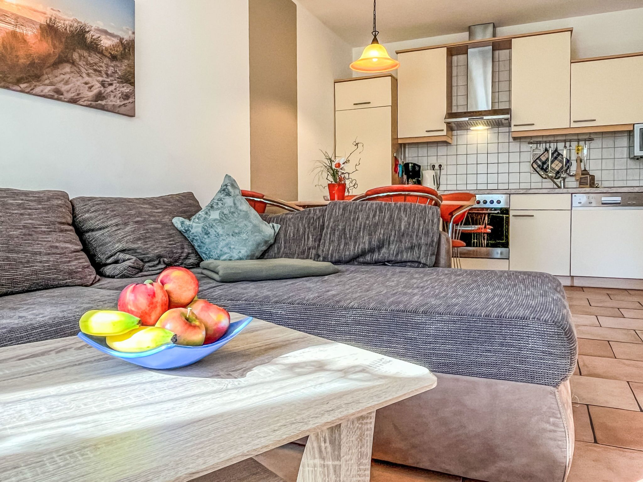 Ein modernes Wohnzimmer mit einer Couch, einem Couchtisch mit Früchten und einer Küche im Hintergrund.