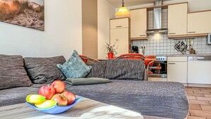 A modern living room with a sofa, a coffee table with fruit, and a kitchen in the background.