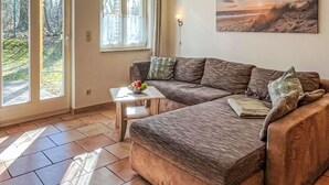 A cozy living room with a sectional sofa, a small table with a bowl of fruit, and a painting of a beach scene.
