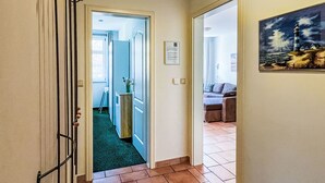 A hallway with a green carpet, a metal rack, and a painting of a lighthouse.