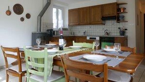 Een eetgedeelte met een houten tafel en stoelen, een keuken met houten kastjes en een fornuis, en een hangende lamp.
