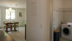 Een kamer met een eethoek, een wasmachine en een deur naar een andere kamer.