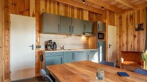 Een keuken met houten wanden, grijze kastjes, een houten eettafel en een blauwe stoel.