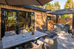 An outdoor patio with a wooden table, chairs, a hot tub, and a pergola.