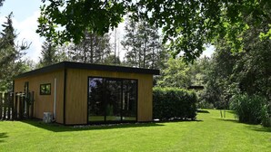 Een modern, laag gebouw met grote glasramen, omgeven door een verzorgd gazon en weelderige bomen.