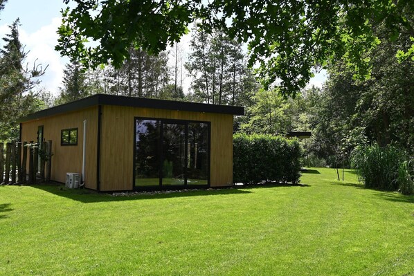 A modern, single-story building with large glass windows, surrounded by a well-maintained lawn and dense trees.