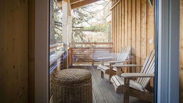 Een houten terras met buitenmeubels, waaronder stoelen en tafels, en een rieten mand.