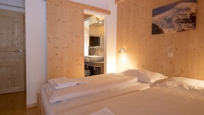 Een kamer met twee bedden, houten wanden, een schilderij en een zichtbare badkamer door een open deur.