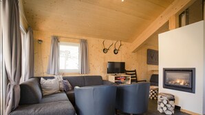 Een gezellige woonkamer met een bank, twee fauteuils, een flatscreen televisie en een open haard.
