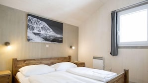 A bedroom with a wooden bed, a mountain painting on the wall, and a window with curtains.
