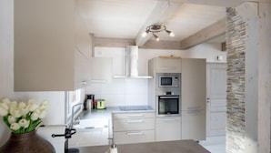 A modern kitchen with white cabinetry, a stone accent wall, and a hanging light fixture.